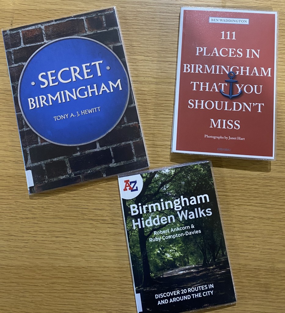 Three books from the Birmingham Collection laid out flat at different angles on a wooden table.