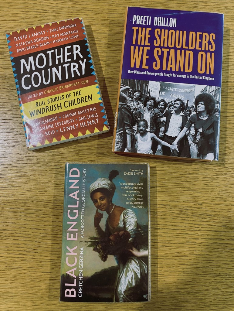 Three books from the Black & South Asian History Collection laid out flat at different angles on a wooden table.