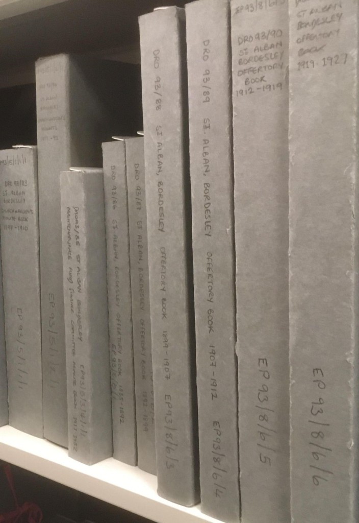 Grey archival boxes on a shelf with writing on the spines