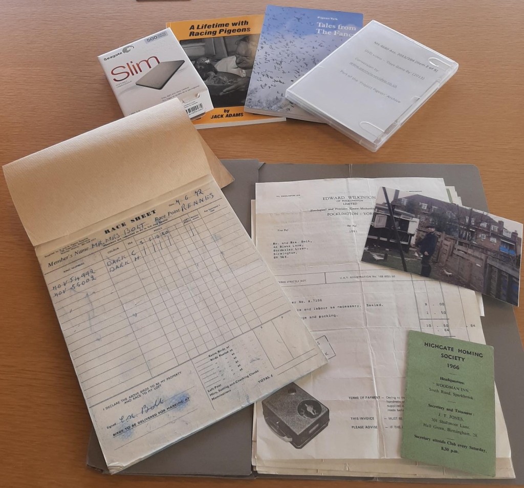 Items grouped on a table including published books, a hard drive, a DVD case, a black and white photograph of a back garden, letters and a race sheet.