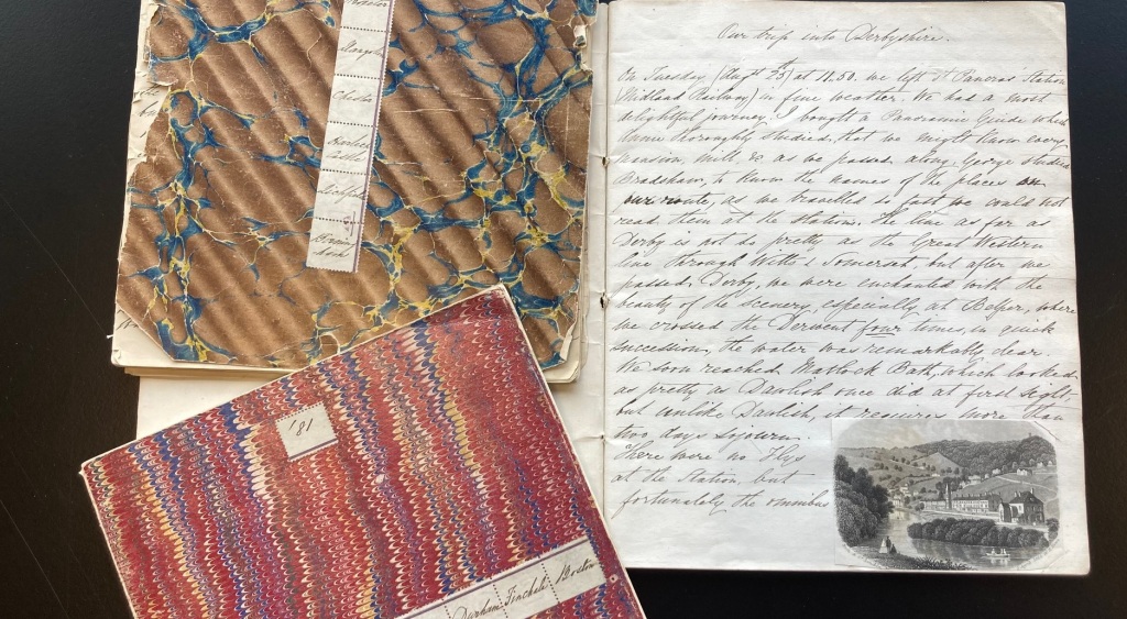 The three diaries laid out, the covers are marbled in bright abtract designs by show signs of damage along the edges, the third diary is open on a page with "A trip into Derbyshire. The main text is too small to read, in the corner a small engraving of a countryside view with a river has been slotted into the page.